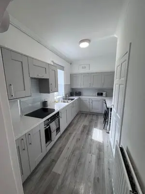 a kitchen with white cabinets and a wooden floor at Helensburgh Central Apartment - Macaulay Letting in Helensburgh