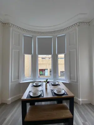 a dining room with a table and two windows at Spacious 2 bed sleeps 5 above traditional music pub in Paisley