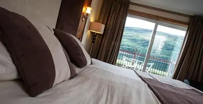 a bed in a hotel room with a large window at Cairndow Stagecoach Inn in Cairndow