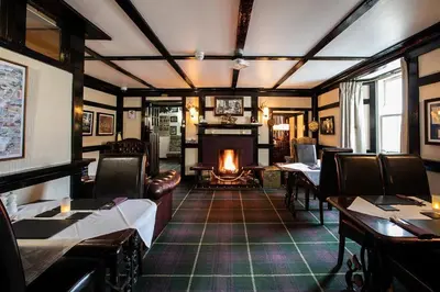 a living room with a fireplace and tables and chairs at Cairndow Stagecoach Inn in Cairndow