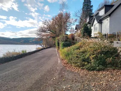a dirt road next to a house and a lake at Ardross Cottage in Aberfoyle