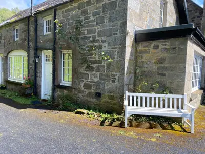 a white bench sitting outside of a stone building at Birch Tree Cottage in Killichonan