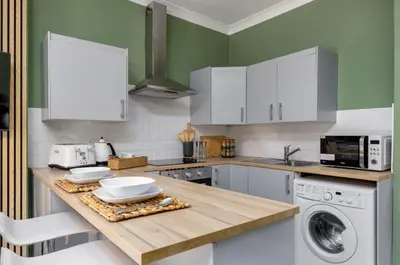 a kitchen with white cabinets and a washer and dryer at Ochill View Apartment by Stirling Train Station in Stirling