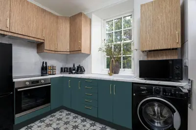 a kitchen with blue cabinets and a washer and dryer at Woodland Hideaway Near Stirling in Cambusbarron