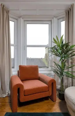 an orange chair in a living room with a window at Stylish Penthouse Retreat in Stirling