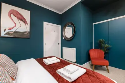 a bedroom with a bed with a red chair and a mirror at Stylish Penthouse Retreat in Stirling