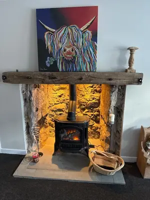 a fireplace with a painting of a cow on the wall at Cosy Wee Cottage in Monkton