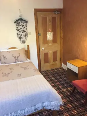 a bedroom with a bed and a table and a door at Tanglin Guest House in Oban