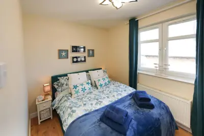 a bedroom with a bed with blue sheets and a window at Caledonia by the Sea in Saltcoats