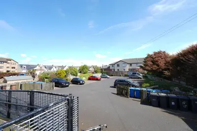 a parking lot with parked cars and trash cans at Caledonia by the Sea in Saltcoats