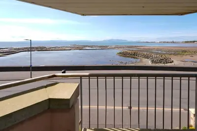 a balcony with a view of a beach and water at Caledonia by the Sea in Saltcoats
