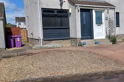 a house with a black door and a gravel driveway at Modern flat in quiet residential cul-de-sac in Kilwinning