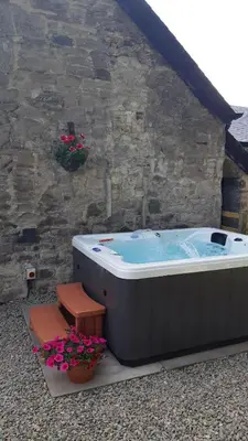 a hot tub sitting next to a stone wall at A Cozy Bothy Retreat with Hot Tub in Keilour