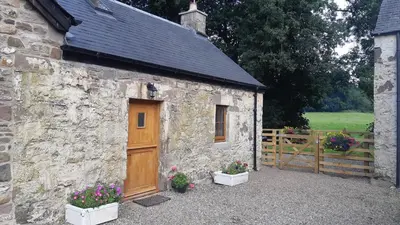 a stone building with a wooden door and some flowers at A Cozy Bothy Retreat with Hot Tub in Keilour
