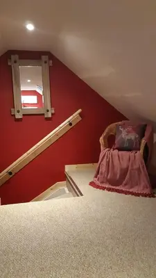 a room with a red wall with a chair and a window at A Cozy Bothy Retreat with Hot Tub in Keilour