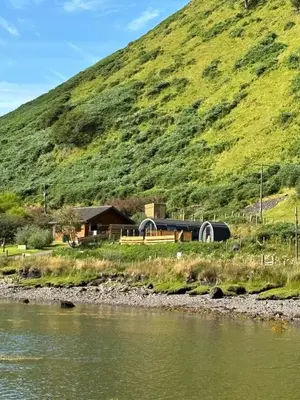 a house on the side of a hill next to a river at Luxury Pod and Sauna with Fantastic Sea Views in Oban