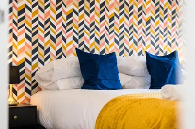 a bed with blue pillows and a colorful patterned wall at Glenfiddich Apartment in Oban