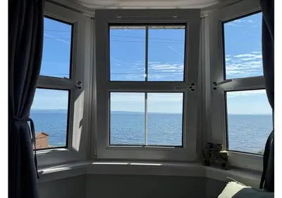 a room with three windows looking out at the ocean at Eldon Cottage in Isle of Arran