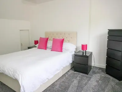 a bedroom with a white bed with pink pillows and a dresser at 3 Whin Bank in Oban