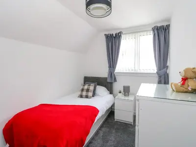 a small bedroom with a red blanket on a bed at 3 Whin Bank in Oban