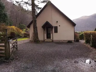 a small white house with a tree in front of it at Lochside Cottage Glencoe