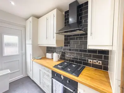 a kitchen with white cabinets and a black stove at Clydebank 2 Bedroom Home in Drumchapel