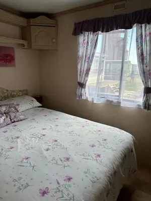a bedroom with a bed with a floral comforter and a window at 27 Glenfinart Caravan Park in Dunoon