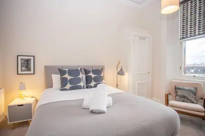 a white bedroom with a large bed and a chair at Spacious Period Property in Glasgow in Glasgow