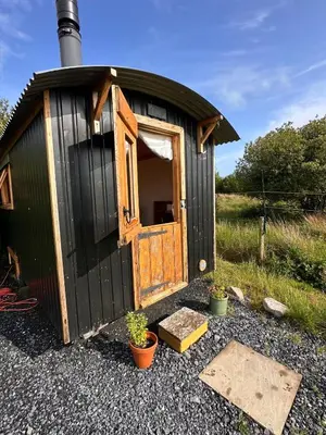 a black shed with a door and some plants at The Shepherd's Hut in Craighouse