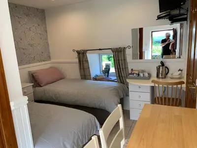 a room with two beds and a table and a mirror at Whitestone Cottage in Turnberry