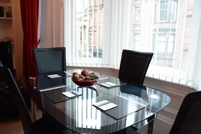 a glass table with chairs and a bowl of fruit on it at Townhead Apartments Glasgow Airport in Paisley