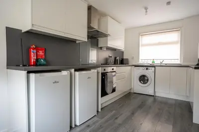 a kitchen with white cabinets and a washer and dryer at Torbrex House in Cumbernauld