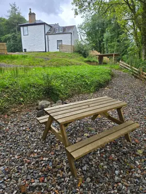 a wooden picnic table sitting on a gravel path in front of a house at Ben Lomond Apartment in Tarbet