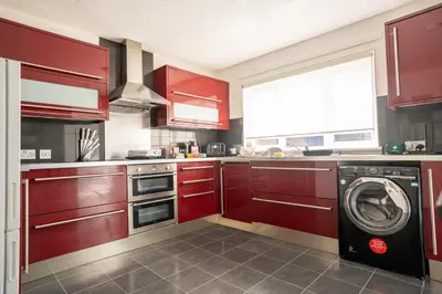 a kitchen with red cabinets and a washing machine at 4 BDR House By Caledonia Luxe Stays Short Lets & Serviced Accommodation Livingston in Livingston