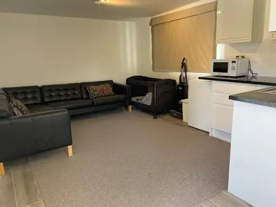 a living room with a black couch and a kitchen at Detached Annexe in Moffat