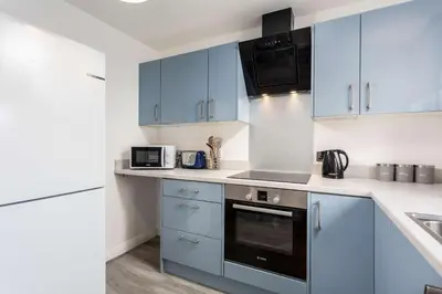 a kitchen with blue cabinets and a stove top oven at Albyn Retreat - Donnini Apartments in Prestwick