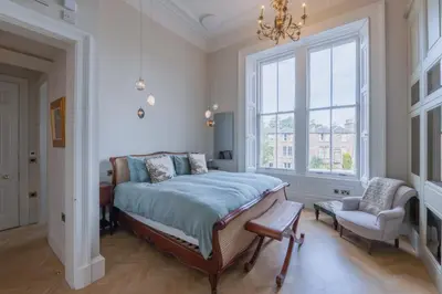 a bedroom with a bed and a chair and a window at Luxury West End flat with stunning bay window views in Edinburgh