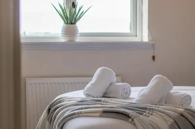 a bed with towels on it with a window at The Well - 3 bedroom apartment in Motherwell