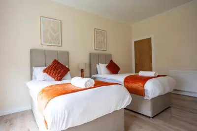 two beds in a room with white and orange sheets at Curtis Apartment in Glasgow