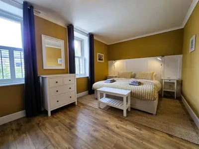 a bedroom with a bed and a dresser and two windows at Balmory Stables South - luxury stable conversion in Ascog