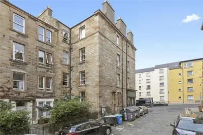 an old brick building with cars parked in a parking lot at Haymarket Edinburgh Flat Sleeps 4 in Edinburgh