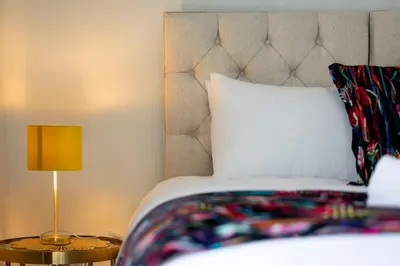 a bed with a white pillow and a table with a lamp at The Burnbank Experience in Glasgow