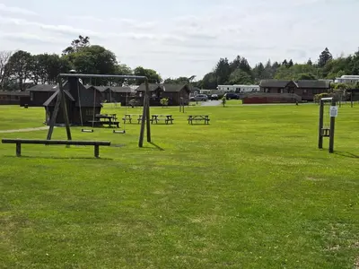 a park with benches and a swing set in the grass at Lovely Caravan number 96 at Three Lochs Holiday Park in Kirkcowan