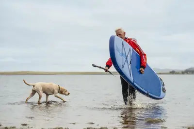 a man walking a dog in the water with a surfboard at Carnethy Cabin in Kirknewton