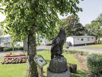 a statue of a bird sitting on a stump next to a tree at Manor Heights Lodge in Wemyss Bay