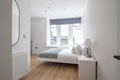 a white bedroom with a bed and a window at Alexandra Apartment in Falkirk