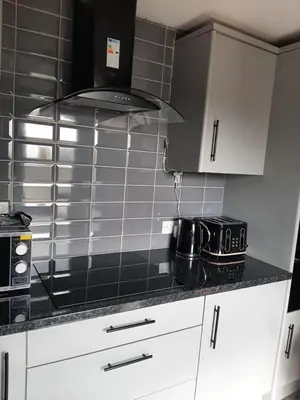 a kitchen with white cabinets and a black counter top at Newly renovated & furnished luxury bedroom in Kirkliston