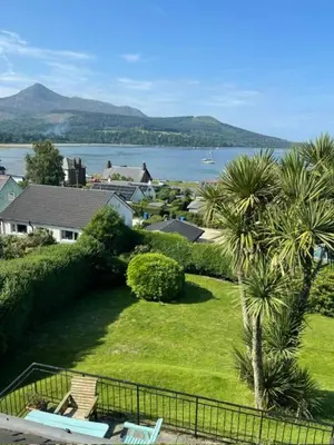 a park with a palm tree and a view of the water at Grey Gables Cottage, Brodick, Isle of Arran, Scotland in Isle of Arran