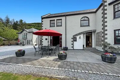 a patio with a table and umbrella in front of a house at The Allanbreck Studio Glencoe Ballachulish Highlands Near Fortwilliam in Glencoe