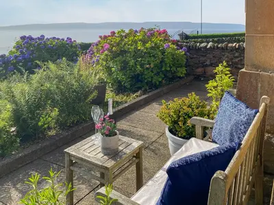 a patio with a bench and flowers and the ocean at Thornlie - Uk49875 in Blairmore